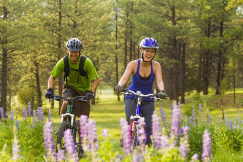 Couple riding mountain bikes in meadow