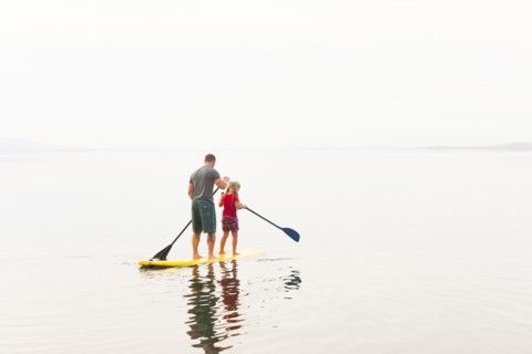 Caucasian father and daughter riding paddle board