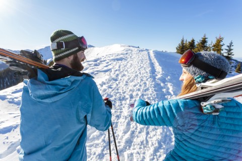 Couple carrying skis on snowy mountain