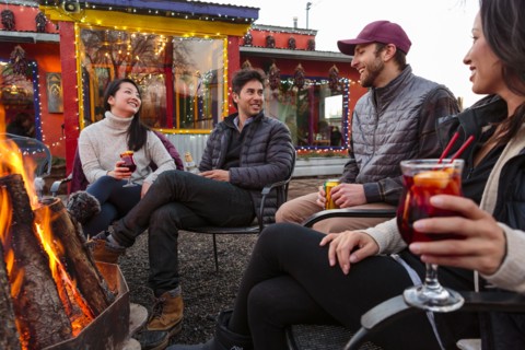Couples drinking cocktails and beer outdoors at storefront campfire