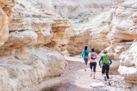 Women running in canyon wearing backpacks