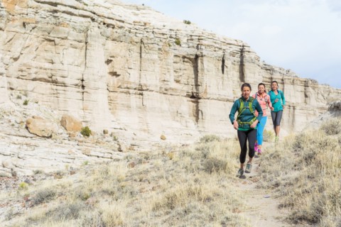 Women running in canyon wearing backpacks