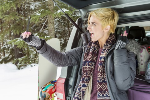 Caucasian woman at car posing for cell phone selfie in winter