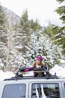 Caucasian woman checking snowboards in car roof rack