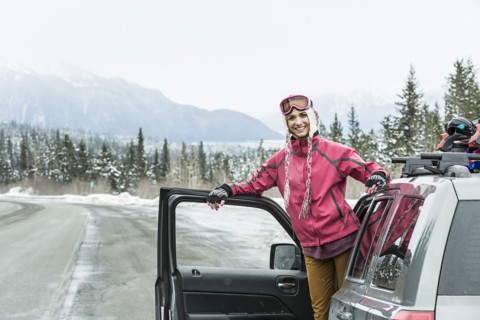 Smiling Caucasian woman standing in car in winter