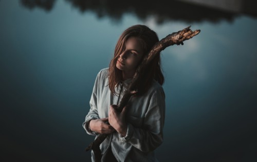 Caucasian woman holding stick near still lake