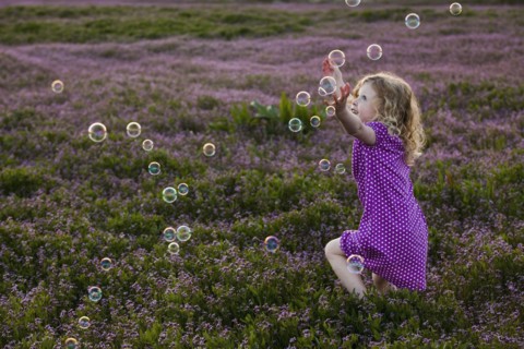 Caucasian girls chasing bubbles in field of flowers