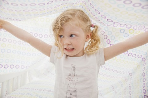 Caucasian girl playing underneath bed sheet