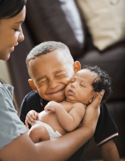 Mixed race boy hugging newborn baby