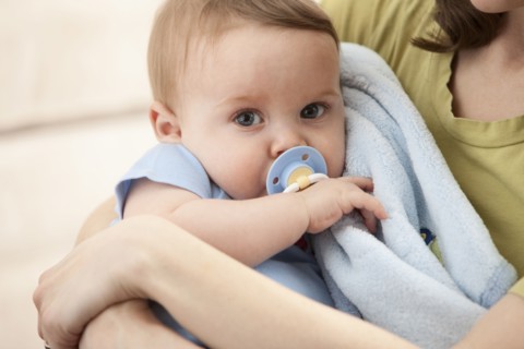 Caucasian baby boy with pacifier in mother's arms