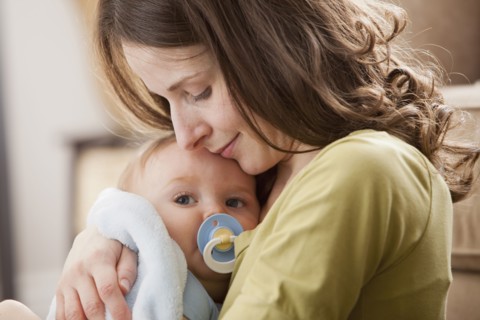 Caucasian baby boy with pacifier in mother's arms