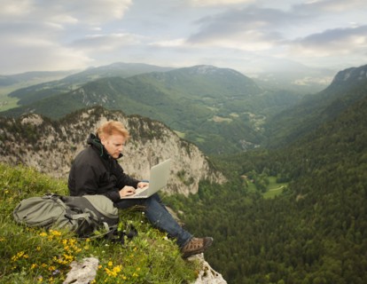 Caucasian man using laptop on remote cliff's edge