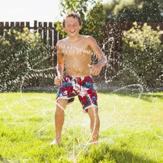 Caucasian boy playing in sprinkler