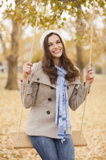 Caucasian woman sitting on swing in autumn leaves