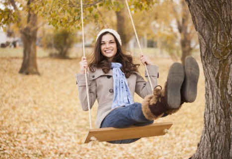 Caucasian woman sitting on swing in autumn leaves