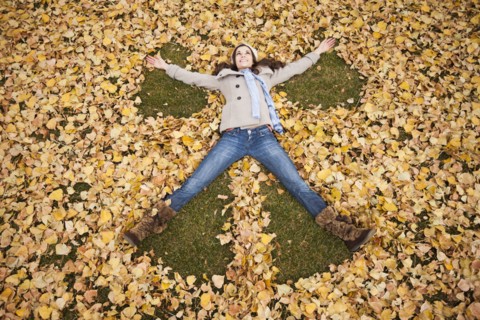 Caucasian woman making angel in autumn leaves