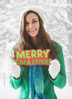 Caucasian woman holding 'Merry Christmas' sign in snow