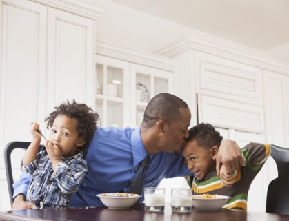Father kissing sons at breakfast table