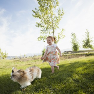 Caucasian girl chasing dog in grass