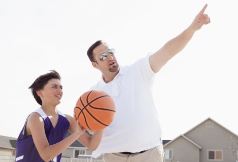 Father teaching son to play basketball in driveway