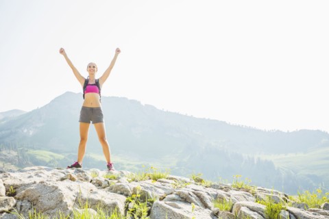 Caucasian woman cheering on rocky hilltop