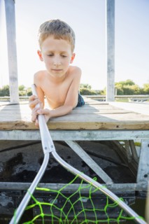 Caucasian boy using fishing net on dock