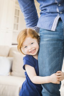 Caucasian girl clutching father's leg