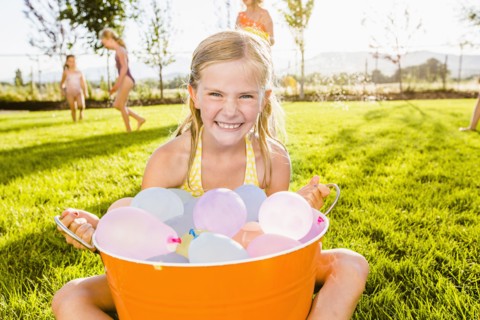 Caucasian girl playing with water balloons in backyard