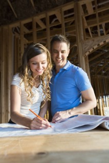 Caucasian couple marking blueprints in house under construction