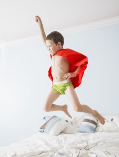 Caucasian boy playing superhero on bed