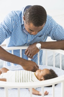 Father admiring sleeping baby son in crib