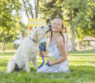 Pet dog licking face of Caucasian girl on grassy lawn