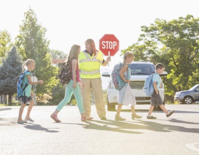 Caucasian crossing guard helping children in crosswalk