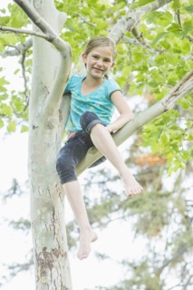 Smiling Caucasian girl climbing tree outdoors