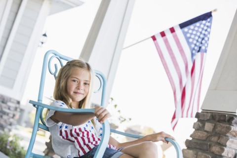 Caucasian girl sitting on porch near American flag