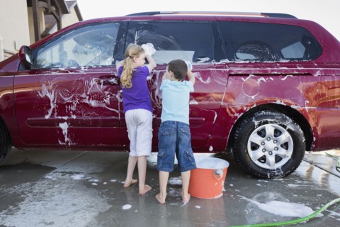 Caucasian children washing car in driveway