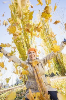 Older Caucasian woman playing in autumn leaves