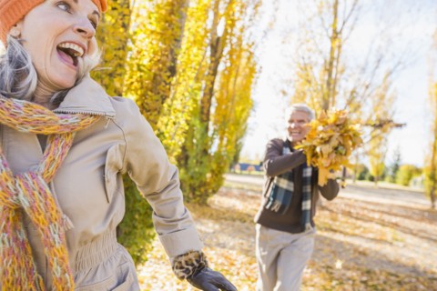Older Caucasian couple playing with autumn leaves