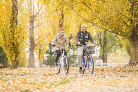 Older Caucasian couple riding bicycles on autumn leaves