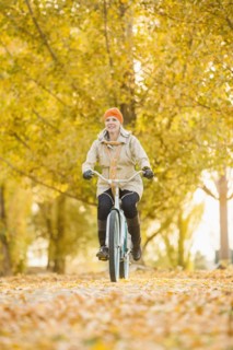 Older Caucasian woman riding bicycle on autumn leaves