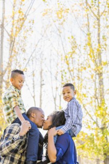 Parents carrying children on shoulders near autumn trees