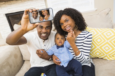 Black family taking selfie on sofa in living room
