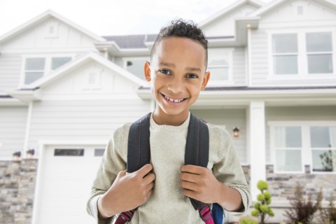 Black boy in backpack smiling outside house