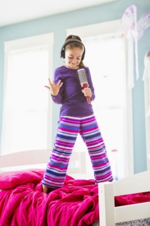 Caucasian girl singing into hairbrush on bed