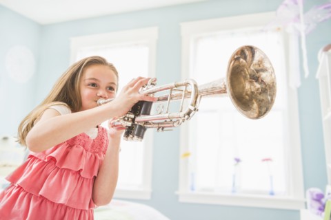 Caucasian girl playing trumpet in bedroom