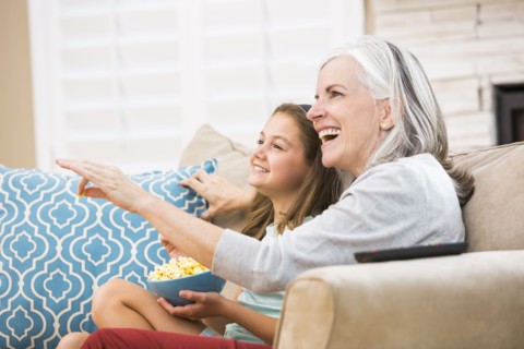 Caucasian grandmother and granddaughter watching television on sofa