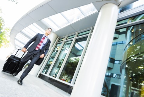 Mixed race businessman rolling luggage in office
