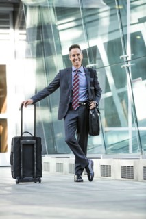 Mixed race businessman rolling luggage outdoors