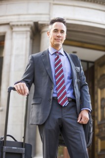 Mixed race businessman rolling luggage outdoors