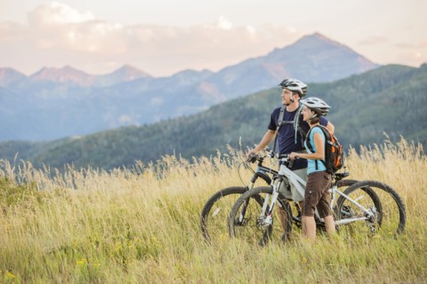 Caucasian couple riding mountain bikes in field